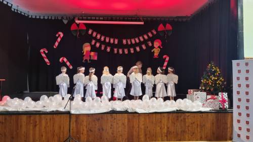 Dzieci na scenie w strojach aniołków, tyłem, śpiewające piosenki
